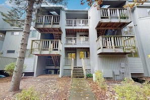 Un edificio de varios pisos con balcones, una terraza de madera y una pequeña entrada.