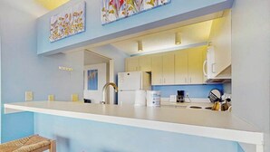 Eine moderne Küche mit weißen Schränken, einer weißen Arbeitsplatte und einem Edelstahlspülbecken. Vor der Arbeitsplatte stehen zwei Korbstühle.