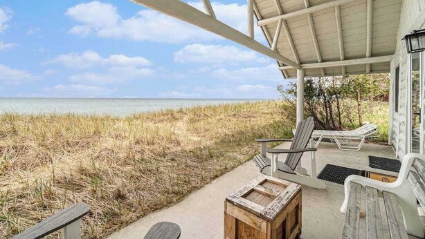 A covered outdoor seating area with chairs and a table, overlooking a beach with tall grass. - Lakefront cabin with 100 ft of Lake Michigan beach, full kitchen, loft, & deck (Empire)