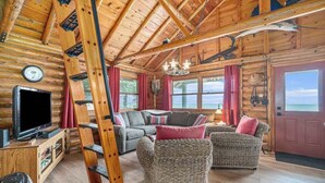A log cabin interior with a television, sofas, a ladder, and a view of the outdoors. - Lakefront cabin with 100 ft of Lake Michigan beach, full kitchen, loft, & deck (Empire)