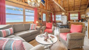 A log cabin interior with a sofa, wicker chairs, a dining table, and a kitchen area. - Lakefront cabin with 100 ft of Lake Michigan beach, full kitchen, loft, & deck (Empire)