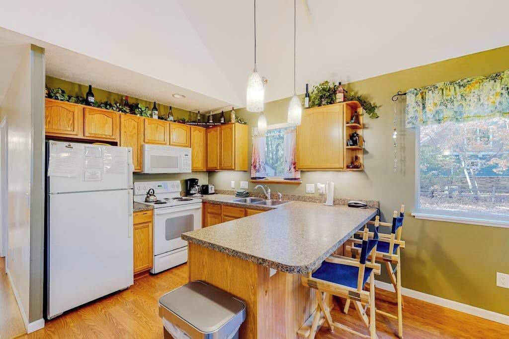 A kitchen with wooden cabinets, a white refrigerator, a microwave, a stove, and a granite countertop island with blue chairs.