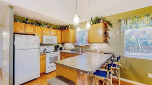 Une cuisine avec des meubles en bois, un réfrigérateur blanc, un four à micro-ondes, une cuisinière et un îlot central en granit avec des chaises bleues.