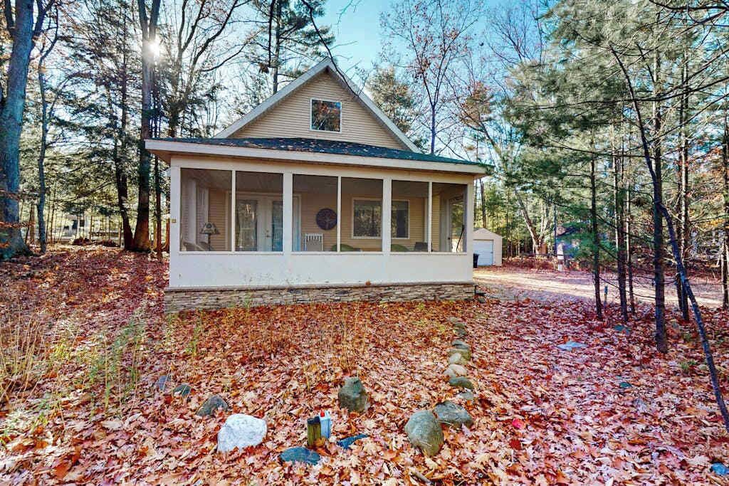 A small, single-story cabin with a porch, surrounded by a forest.
