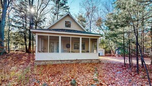 Une petite cabane à un seul étage, dotée d’un porche et entourée d’une forêt.