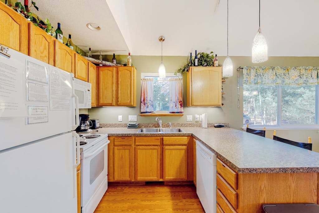 A kitchen with wooden cabinets, a white refrigerator, a stove, a sink, and pendant lights.