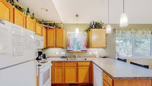 Une cuisine avec des meubles de rangement en bois, un réfrigérateur blanc, une cuisinière, un évier et des luminaires suspendus.