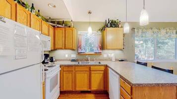 A kitchen with wooden cabinets, a white refrigerator, a stove, a sink, and pendant lights.