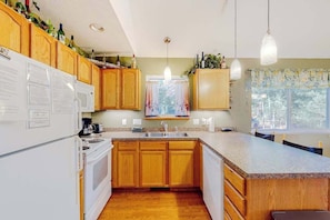 A kitchen with wooden cabinets, a white refrigerator, a stove, a sink, and pendant lights. - Welcoming home in Downtown Glen Arbor with firepit, fireplace, washer/dryer (Glen Arbor)