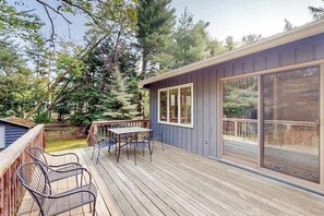 A deck with outdoor furniture, a sliding glass door, and a view of trees. - Dog-friendly downtown Glen Arbor home with deck, gas grill, and washer/dryer (Glen Arbor)
