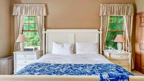 Un dormitorio con una cama, dos mesitas de noche, una lámpara y cortinas.