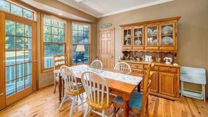 Un comedor con una mesa y sillas de madera, un mueble aparador con puertas de vidrio y una puerta que da al exterior.