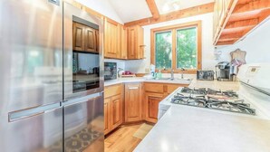 A modern kitchen with stainless steel appliances, wooden cabinets, and a large window providing natural light. - Peaceful, two-story home with a firepit & washer/dryer - close to the beach (Empire)