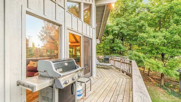 A wooden deck with a grill, a glass door leading to a room, and a view of trees. - Peaceful, two-story home with a firepit & washer/dryer - close to the beach (Empire)