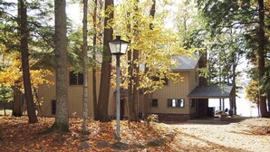 A house surrounded by trees with a porch and a lamp post. - Newly remodeled waterfront home on Little Glen Lake with deck, gas grill, AC (Empire)