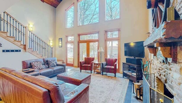 A spacious living area with a staircase, leather sofas, a fireplace, and large windows. - Newly remodeled waterfront home on Little Glen Lake with deck, gas grill, AC (Empire)