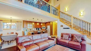 A spacious living area with a high ceiling, a dining table, a sofa, and a staircase. - Newly remodeled waterfront home on Little Glen Lake with deck, gas grill, AC (Empire)