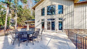 A building with a patio area featuring a table and chairs, large windows, and a stone foundation. - Newly remodeled waterfront home on Little Glen Lake with deck, gas grill, AC (Empire)