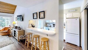 A modern kitchen with a bar area, white cabinets, and a refrigerator. - Riverfront condo with lake access, views, deck, washer/dryer, community firepit (Glen Arbor)