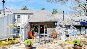 A house with a patio, outdoor seating, and potted plants. - Riverfront condo with lake access, views, deck, washer/dryer, community firepit (Glen Arbor)