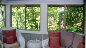 A room with a white wicker sofa and armchair, a small white side table, and a window with a view of trees. - Spacious lake access home with a washer/dryer, central AC, nearby tennis (Glen Arbor)