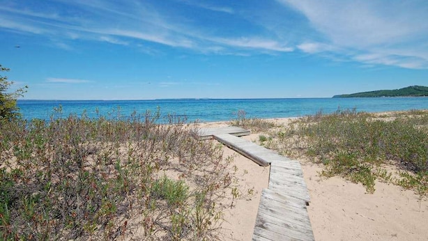 A sandy beach with a wooden boardwalk leading to the water, surrounded by sparse vegetation. - Spacious lake access home with a washer/dryer, central AC, nearby tennis (Glen Arbor)