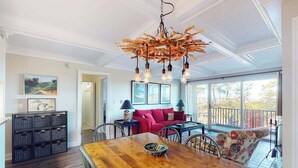 Un coin repas avec une table en bois, des chaises et un lustre. On y trouve également un canapé rouge et un balcon avec une balustrade.