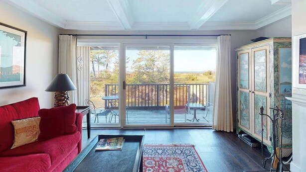 Un salon avec un canapé rouge, une table basse, une lampe, un meuble et une porte-fenêtre coulissante donnant sur une terrasse extérieure.
