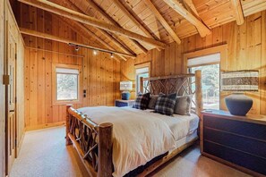 A wooden cabin bedroom with a bed, a nightstand, and a window.