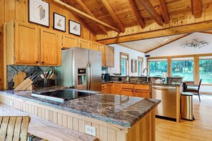 A kitchen with wooden cabinets, granite countertops, stainless steel appliances, and large windows.