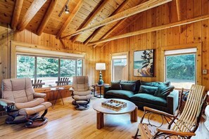 A wooden interior with a sofa, chairs, a coffee table, and large windows.