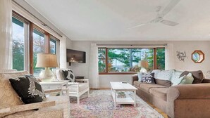 A living room with a sofa, armchair, coffee table, and a TV. - Spacious, airy home near Little Glen Lake with gas grill, deck, and new firepit (Empire)