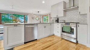 A modern kitchen with white cabinetry, a stainless steel oven, and a window with a view of trees. - Spacious, airy home near Little Glen Lake with gas grill, deck, and new firepit (Empire)
