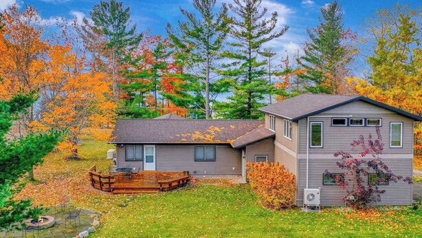 A two-story house with a covered porch, a small deck, and a stone fire pit. - Spacious, airy home near Little Glen Lake with gas grill, deck, and new firepit (Empire)