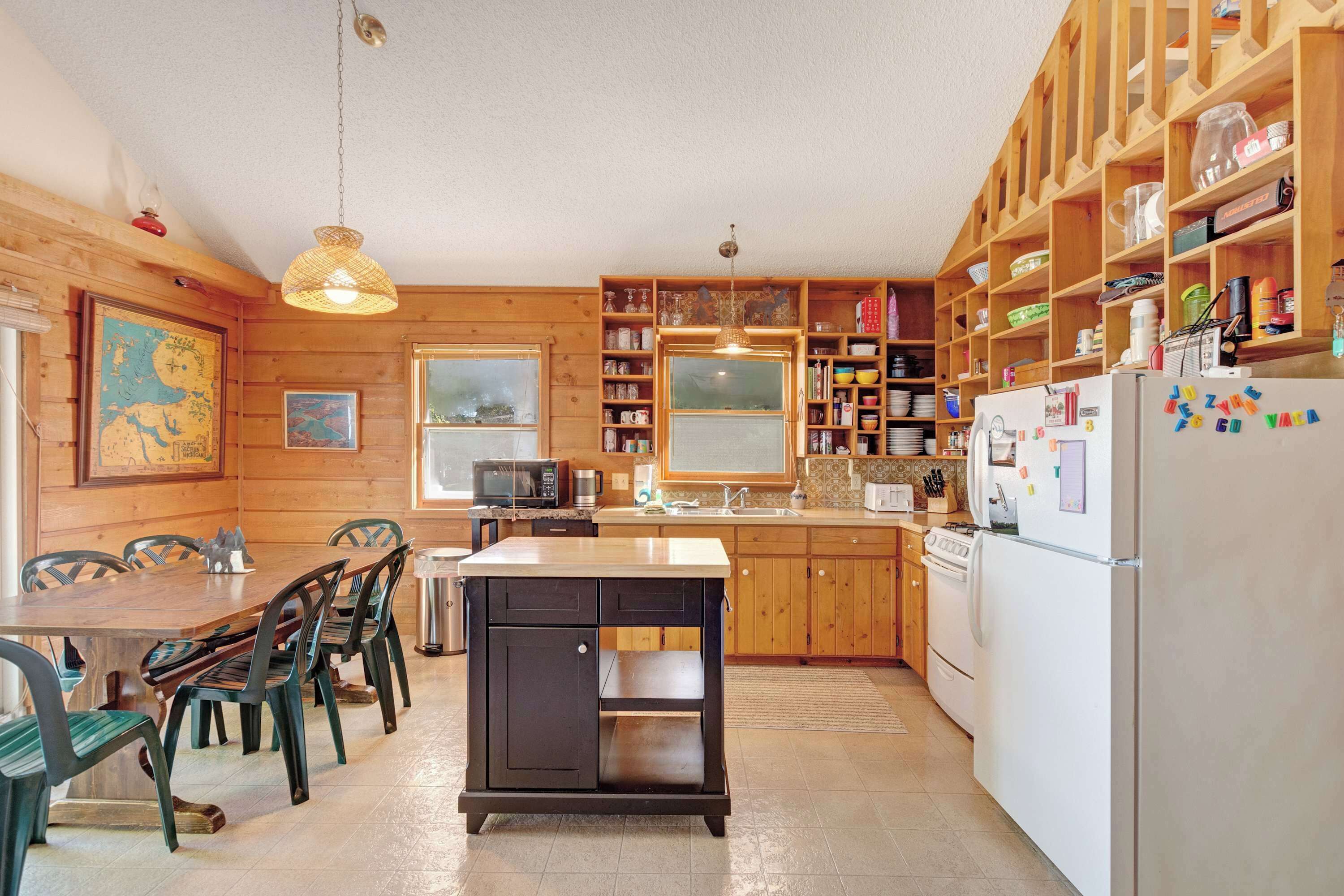 Een keuken met houten kasten, een eettafel met stoelen, een koelkast en een hangende lamp.