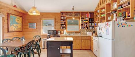 Een keuken met houten kasten, een eettafel met stoelen, een koelkast en een hangende lamp.