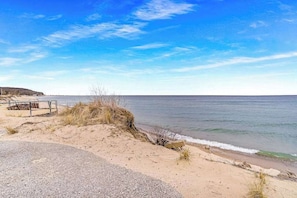 A coastal road with a metal guardrail, sandy dunes, and a clear view of the sea.