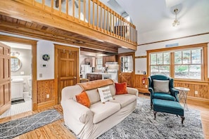 A spacious living area with a high ceiling, wooden beams, a sofa, a chair, and a view of the outdoors.