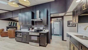 Une cuisine moderne avec des meubles de couleur sombre, des appareils électroménagers en acier inoxydable et des luminaires suspendus.