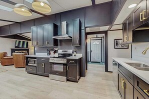 A modern kitchen with dark cabinetry, stainless steel appliances, and pendant lighting.