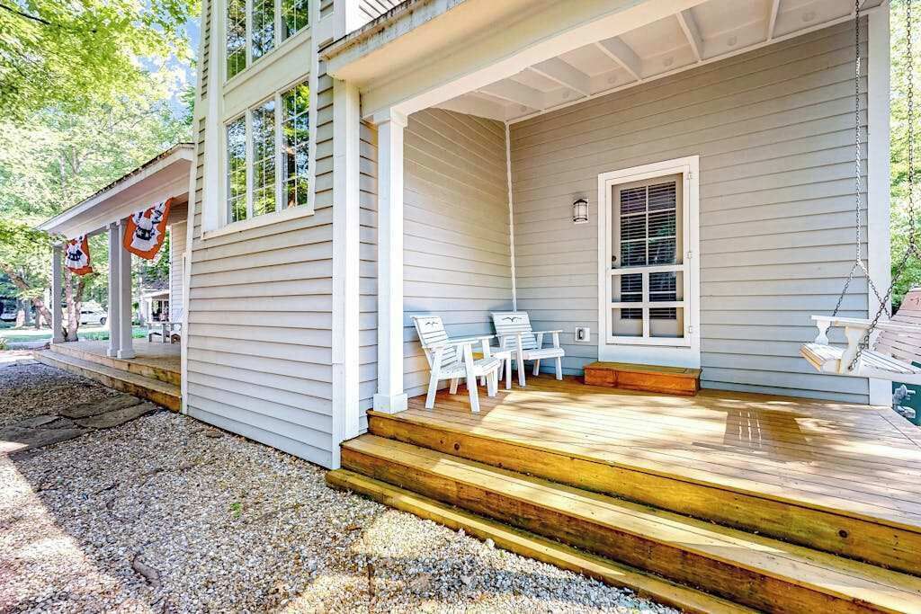 Une maison avec un porche, des marches et deux chaises blanches.
