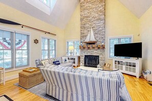 A living room with a stone fireplace, a television, and a striped sofa. - Newly-updated grand home in Union Pier‚Äôs Lakeshore Cottages with pool (Union Pier)