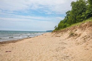 A sandy beach with gentle waves, a grassy cliff, and a clear sky. - Newly-updated grand home in Union Pier‚Äôs Lakeshore Cottages with pool (Union Pier)