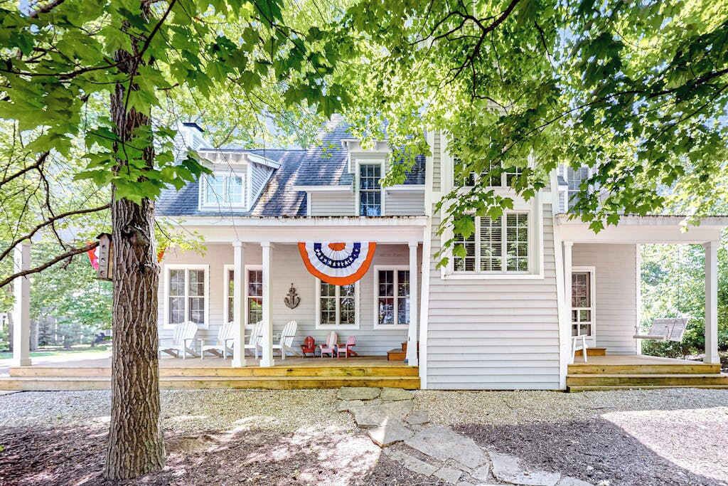 A two-story house with a porch, a flag, and a tree.