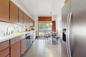A kitchen with wooden cabinets, a stainless steel refrigerator, a dining table with chairs, and a window with a view of greenery. - Rustic beach cottage with partial lake views, grill, & WiFi - great location (Michiana)