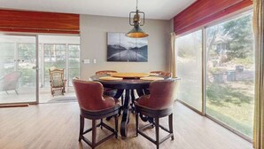 A dining area with a round table, four chairs, a hanging light fixture, and a large window with a view of the outdoors. - Rustic beach cottage with partial lake views, grill, & WiFi - great location (Michiana)