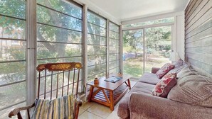 A sunroom with large windows, a wooden bench, a sofa, and a small table. - Rustic beach cottage with partial lake views, grill, & WiFi - great location (Michiana)