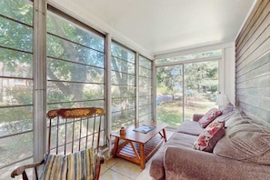 A sunroom with large windows, a wooden bench, a sofa, and a small table. - Rustic beach cottage with partial lake views, grill, & WiFi - great location (Michiana)