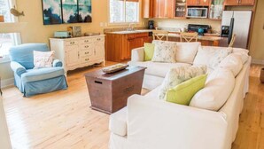 Un salon avec un fauteuil bleu, un canapé blanc et une table basse en bois.