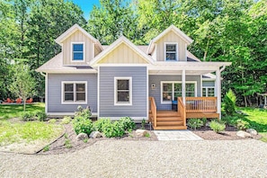 A two-story house with a covered porch, a front yard with landscaping, and a gravel driveway.